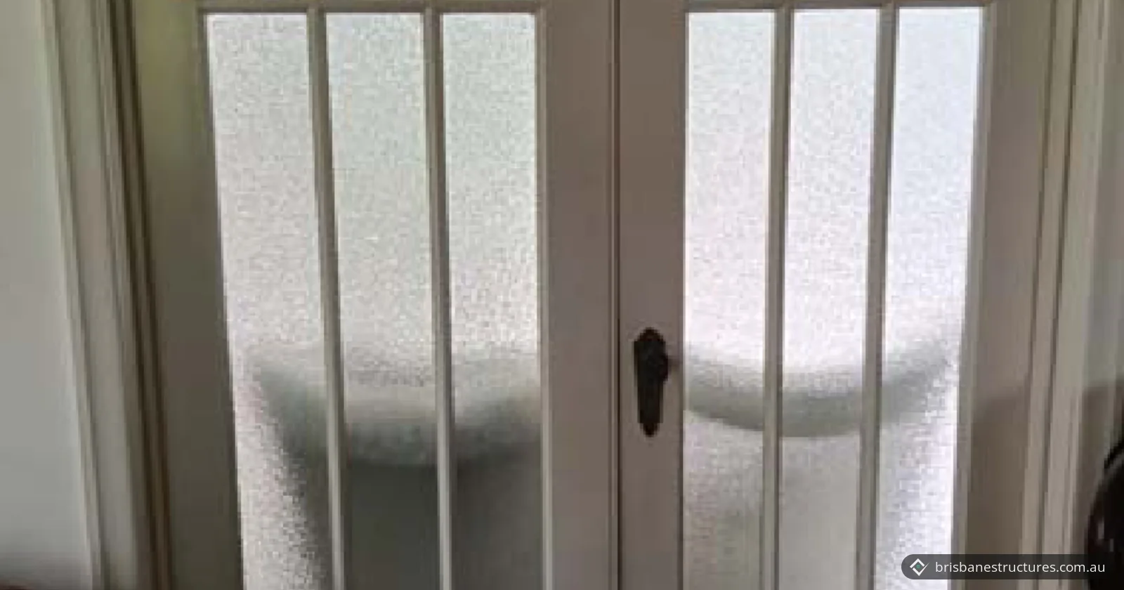 Closed white double French doors with frosted glass panes and a dark door handle